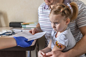 Little girl with her father in the doctor's office at the clinic. Vaccinated against coronavirus....