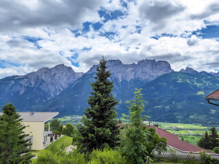 A distanced view on sharp and stony mountain range of Lienz Dolomites, Austria. The slopes are barren, with little grass on it. Dangerous mountain climbing. Few rooftops below. Natural beauty
