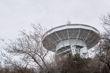 mirror of the astronomical radio telescope, aimed at the sky, is visible from the trees