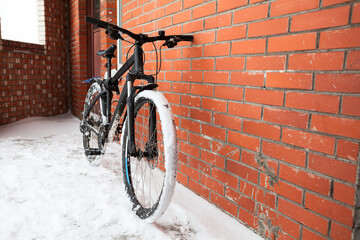 Fototapeta na wymiar Modern mountain bicycle leaning to red brick wall, snow covered wheels, winter time