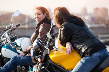 Fototapeta na wymiar Two European women motorcyclists talking cheerfully while sitting on their motorcycles