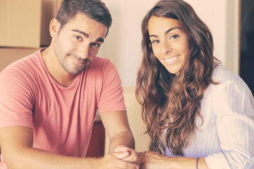 Happy cheerful man and woman enjoying moving into new house, standing indoors, leaning on carton box, looking at camera and smiling. Medium shot. New home concept
