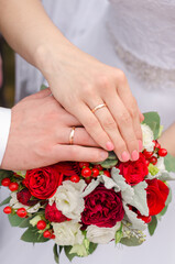 Hands of the bride and groom with wedding rings on the background of the wedding bouquet. Close-up.