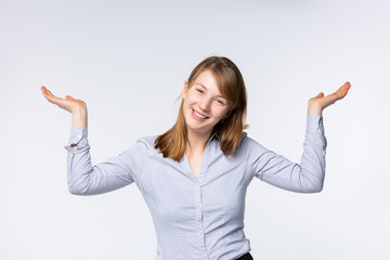 Studio portrait of a happy young blonde, raising her hands in a gesture of uncertainty, shrugging, not knowing what to choose, smiling happily, sitting on a white background