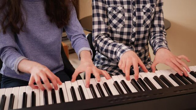 Teenage girls twin sisters at home play electronic piano in four hands during music rehearsal