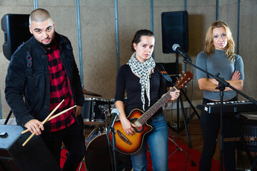 Fototapeta na wymiar Three happy cheerful bandmates posing together with musical instruments in rehearsal room