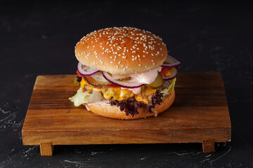 Burger with beef, cheese, onions, pickles and sauce with a white  bun on a dark background.