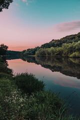 Morning sunrise with pink cotton candy skies and glass like reflections, wildflowers and lush green grass on a summer morning along the Maquoketa River in Iowa, USA.