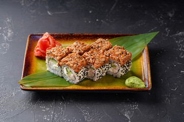 Sushi Сrab and eel rolls on a rectangular plate on a dark background. Decorated with wasabi bamboo leaf and ginger.