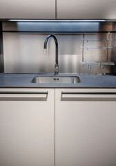 Stainless sink and faucet set against light grey surfaces. Trendy modern kitchen made with light beige and grey colors. High quality photo