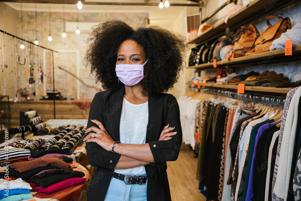 Wall mural Portrait of a beautiful female sales assistant at the entrance of the business with her arms folded - Self-confident millennial owner starts a new business during the Coronavirus Covid-19 pandemic