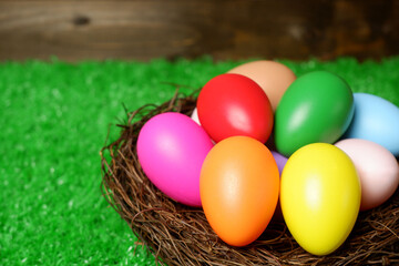 Multi colored easter eggs in birds nest on green grass and wooden panks background closeup view selective focus with copy space. Easter holiday banner, card, poster, voucher, invitation template