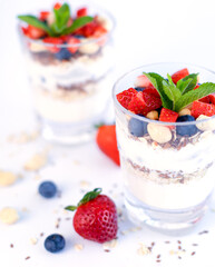 Healthy breakfast of strawberry parfait made with fresh fruit, yogurt, blueberries, flax seeds and muesli, white background. Small depth of field with selective focus on the glass jar in front.
