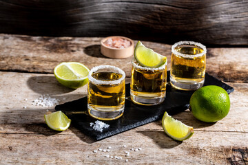 Three tequila shot glasses with salt and lime Mexican national drink. Golden tequila shots. space...