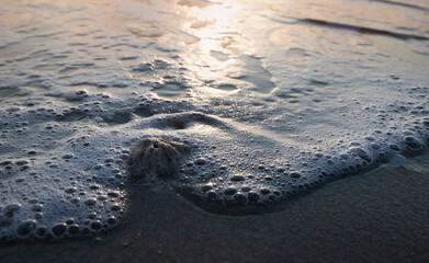 Closeup white bubble sea wave moving ,blurred Sea beach in morning time,reflection of sunrise shining around,
