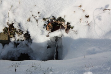 Wasserablauf in einem mit Schnee bedeckten Graben