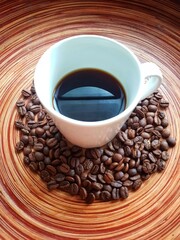 Coffee cup on circular wooden table with coffee beans.