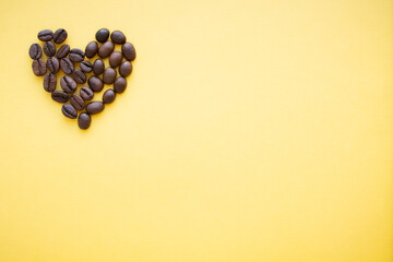 Heart made of coffee beans lies on a yellow background