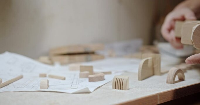 Craftsman assembling wooden toy in workshop. Side view closeup of crop anonymous carpenter making handmade wooden toy at table with details and paper draft in workshop