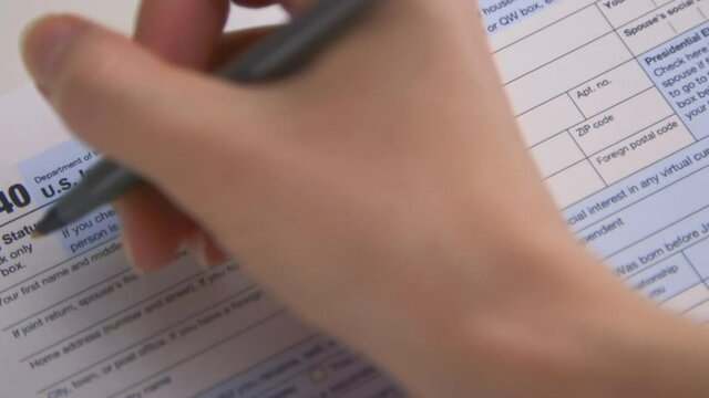 A caucasian woman's hand filling out her name on Tax Form 1040 for tax year 2020, for the IRS. (Camera Used: Canon C300)