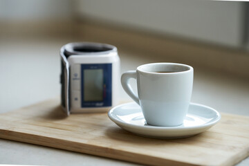  A hand-held blood pressure monitor next to a coffee cup in a home kitchen. Selective focus.
