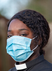 England, UK, December 2020. A black minister wearing a protective medical mask and white collar...
