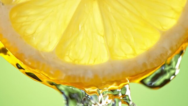 Super Slow Motion Macro Shot of Flowing Water from Lemon Slice on Green Background at 1000fps.