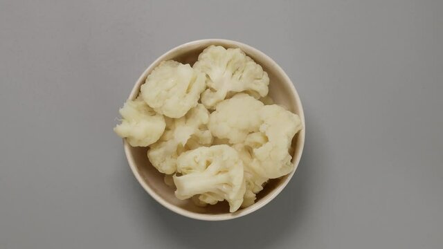 Boiled cauliflower in a bowl on the kitchen table. Womanish hands take a plate from the table for cooking