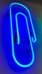 Blue office clip shaped neon light installed on white wall