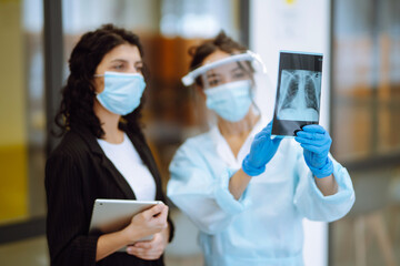 A female doctor in visor and protective gloves  discussing an x-ray. Doctor  examines an X-ray of a...