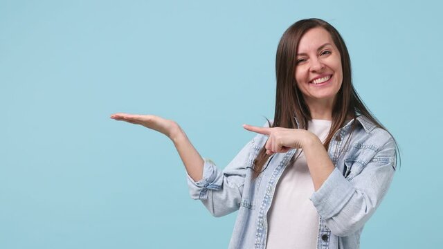 Woman promoter 30s years old in denim jacket white t-shirt recommend suggest select advert point finger aside on workspace copy space mock up promo commercial area isolated on pastel blue background