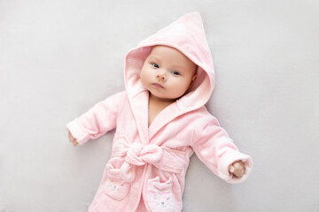 Baby girl in a Terry robe and diaper after bathing. Kid in a hood. Cute happy laughing baby girl in pink soft robe after bath. Baby in a clean and dry towel.