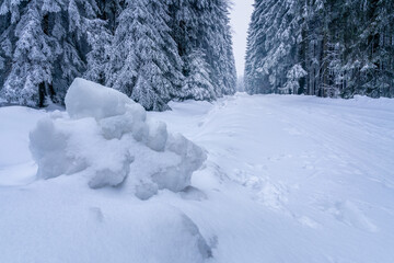 Narrow straight road through frozen winter forest with big ice boulder in the foreground. Cold winter in the Carpathian mountains.
