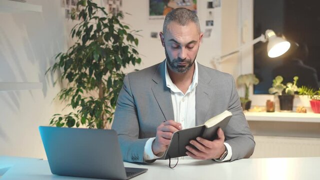 Serious businessman making notes in a notebook while working at home. High quality 4k footage