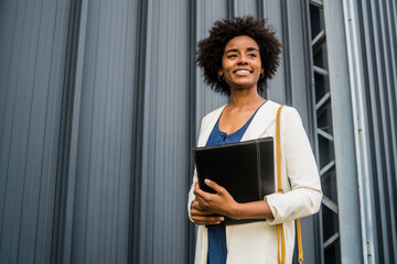 Afro businesswoman holding clipboard outdoors at the street.