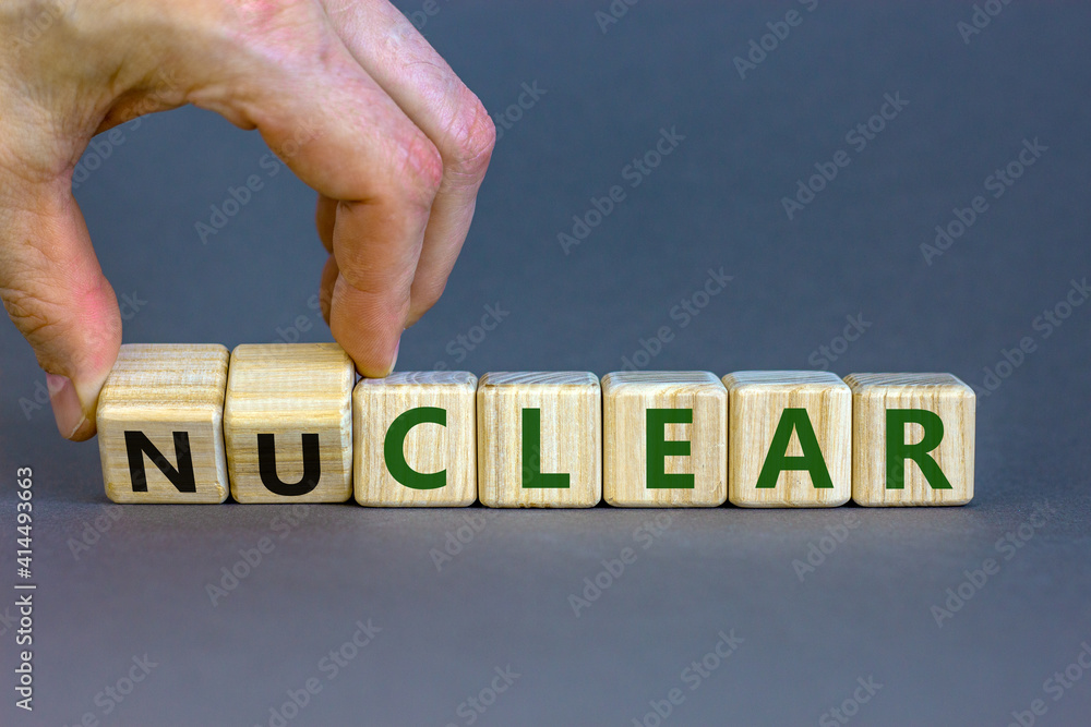 Wall mural Nuclear or clear symbol. Businessman turns a cube and changes the word 'nuclear' to 'clear'. Beautiful grey background. Nuclear or clear and business concept. Copy space.