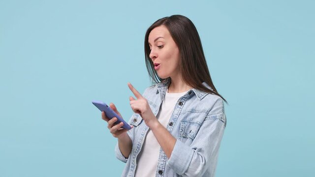 Young woman 30s years old in denim jacket white t-shirt hold use mobile cell phone typing browsing chatting send sms doing online shopping order booking tour isolated on pastel blue background studio