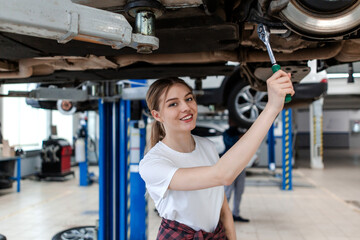 Fototapeta na wymiar Car mechanic girl making car repairs on a lift in a car service station