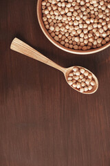 Dry chickpeas in a wooden plate and spoon on a brown wooden background. Top view. Copy, empty space for text