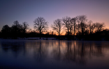 Obraz premium Spiegelung von Bäumen in einem gefrorenen See im Abendrot 