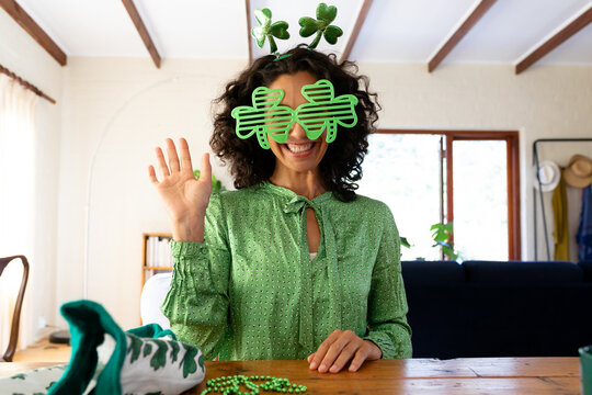 Caucasian woman dressed in green with shamrock glasses for st patrick's day waving during video call