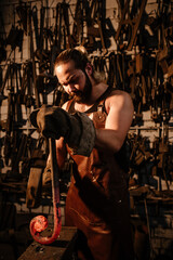 Fototapeta na wymiar Muscular brutal blacksmith in a leather apron in the forge knocks with a hammer on a shattered iron, vertical photo
