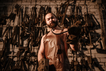 Fototapeta na wymiar Muscular brutal blacksmith in a leather apron works in the forge