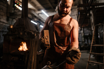 Fototapeta na wymiar Blacksmith in a leather apron in a forge forging anvils with an iron bar