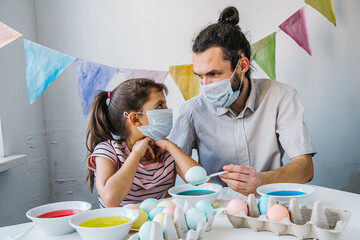 New normal Easter celebration lifestyle concept. Cute little girl and her dad wearing protective...