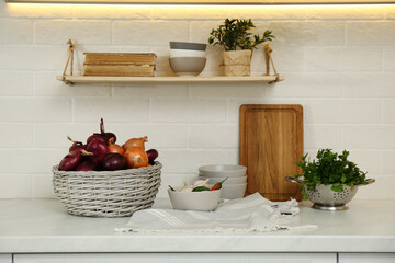 Fresh onions in basket and different kitchenware on countertop indoors