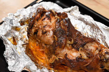 baked meat and fried onions on a baking sheet, pork ham on foil and wooden background, home cooking