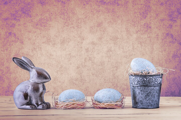 Ein Metall Hase mit drei blaue Eier, Stroh und Metallkübel auf einem Holztisch
