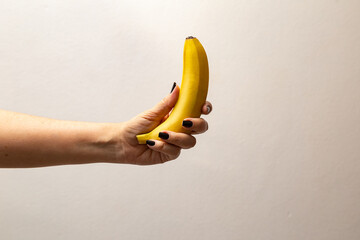 Mão feminina com unhas pintadas de preto segurando uma banana.