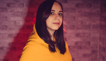 Fototapeta premium A young woman in a fashionable yellow hoodie. Portrait of a beautiful brunette in a yellow hoodie against a brick wall